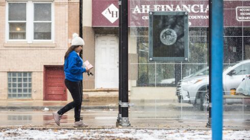 A pedestrian walks along West 18th Street in the Pilsen neighborhood as snow accumulates on the grass at Harrison Park, Tuesday, Nov. 15, 2022. The first projected snowfall for 2023 is on Halloween.