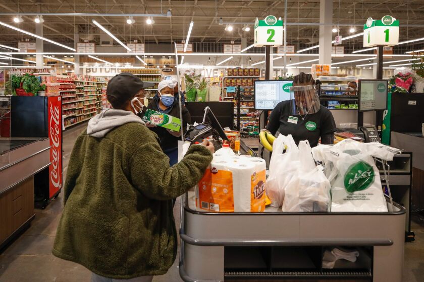 A cashier wearing a face shield bags groceries for a customer in Chicago.