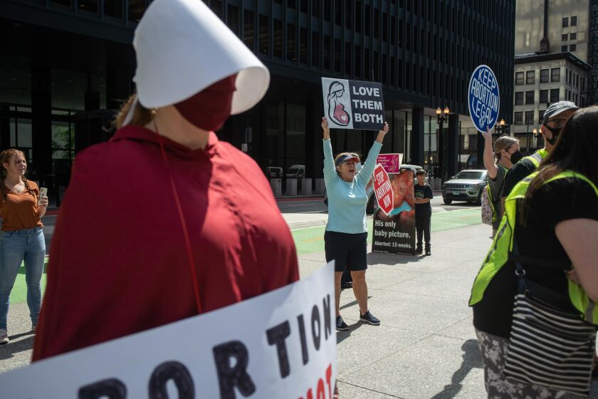 A member of the Illinois Handmaids holds a sign as Rita Sweeney, a member of Pro-Life Action League, yells at attendees during the “Bans Off My Body” rally Friday afternoon at Federal Plaza in the Loop.