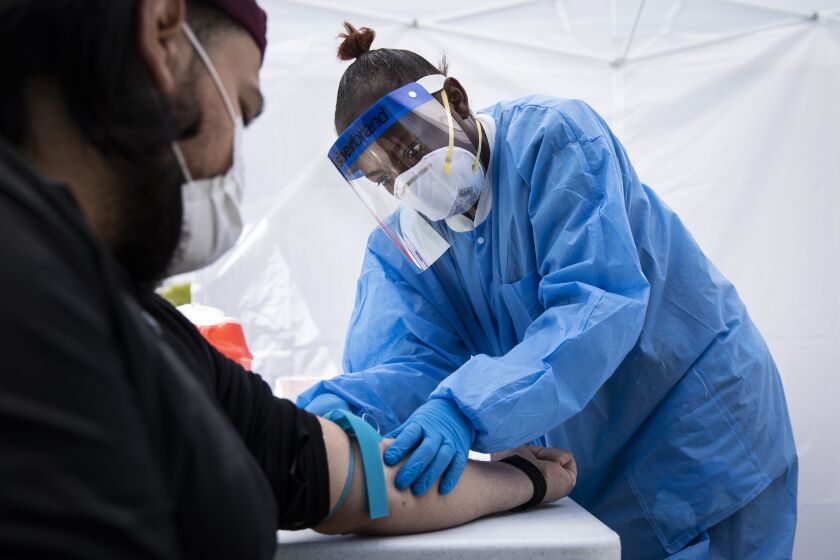 Phlebotomist Crystal Bovan, with Simple Laboratories, draws blood for coronavirus antibody testing for a man at the lab’s drive-thru testing site in the parking lot of St. Rosalie Catholic Parish in Harwood Heights, Friday, May 1, 2020.