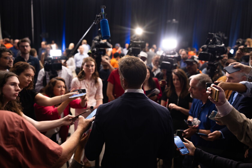 Secretary of State Alexi Giannoulias's back is to the camera with a dozen reporters holding microphones and cameras in front of him as he speaks to the press after announcing his run for mayor.
