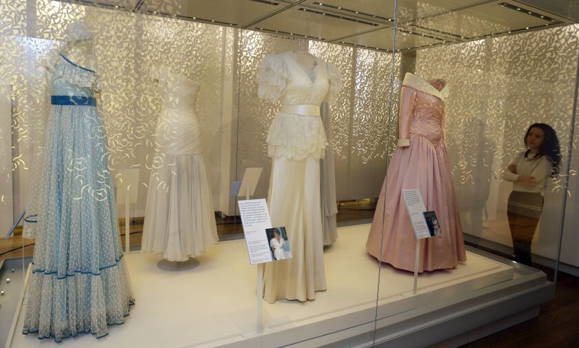 A member of staff at Kensington Palace looks at a selection of dresses including at centre a dress by Bruce Oldfield of satin and lace over bodice and worn by Diana, Princess of Wales in 1990 at the Courtauld Institute of Art and a State Banquet at Buckin