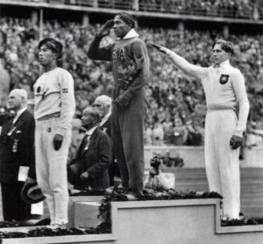 Jesse Owens, center, salutes on August 11, 1936, after defeating Nazi Germany’s Lutz Long, right, in the long jump in the 1936 Summer Olympics in Germany.
