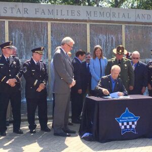 Gov. Bruce Rauner signs a bill that creates a new Illinois Lottery scratch-off game with proceeds to go towards police memorials at the Chicago Police Memorial in front of Soldier Field on Monday. House Republican Leader Jim Durkin and police officers att