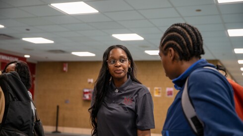 A Black woman wearing glasses speaks with a classmate at her college.