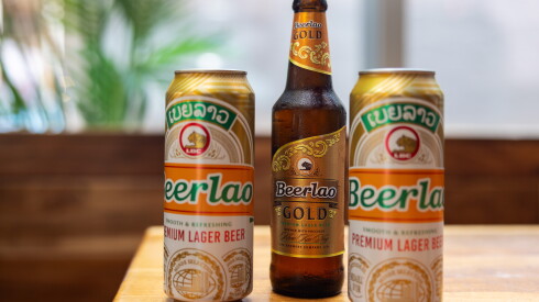 Two tall cans and a bottle of Beerlao on a wooden table.