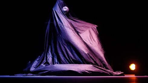 Dancer Nejla Yatkin appears in a dark room beneath a heavy cloak of black fabric as part of her work, "The Other Witch."