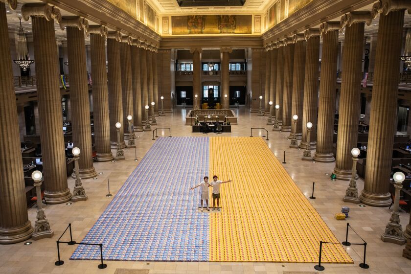 Michael Kotcher, 15, right, and Ryder Shiffman, 16, left, stand in the middle of a Ukrainian flag Thursday that was formed out of cereal boxes at Wintrust’s Grand Banking Hall in the Loop.