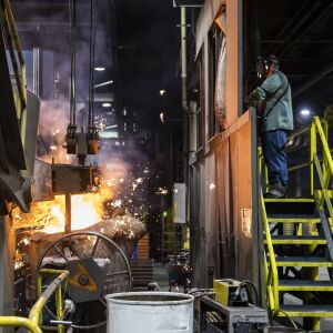 Melt operator Tylar Johnson watches from a safe distance as molten iron pours from a blast furnace into a transfer ladle that will be used to move the glowing metal toward the waiting molds at the Neenah Foundry in Neenah, Wisconsin, Friday, April 8, 2022.