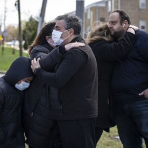 Close friends of Chicago Police Officer Marco DiFranco, who had to stand outside during the funeral amid fears of the coronavirus pandemic, hug each other as the hearse leaves Cumberland Funeral Chapels and heads toward the cemetery, Thursday, April 9, 2020.