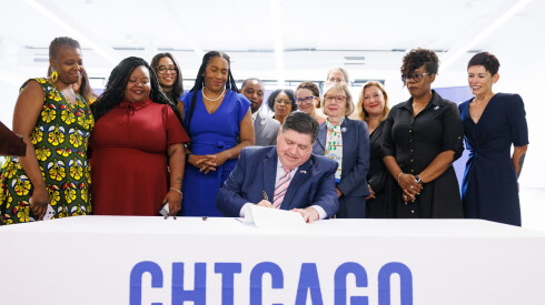 Gov. JB Pritzker sits at a table and signs the Birth Equity Initiative law at Chicago Beyond in West Loop on July 29, 2024. Beside him is Lt. Gov. Juliana Stratton, who led the push for the law.
