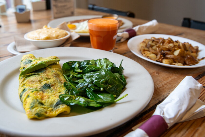 A plate with an omelete and side of spinach sits on a table at Wishbone. There's also a plate of potatoes and a glass of fresh juice.
