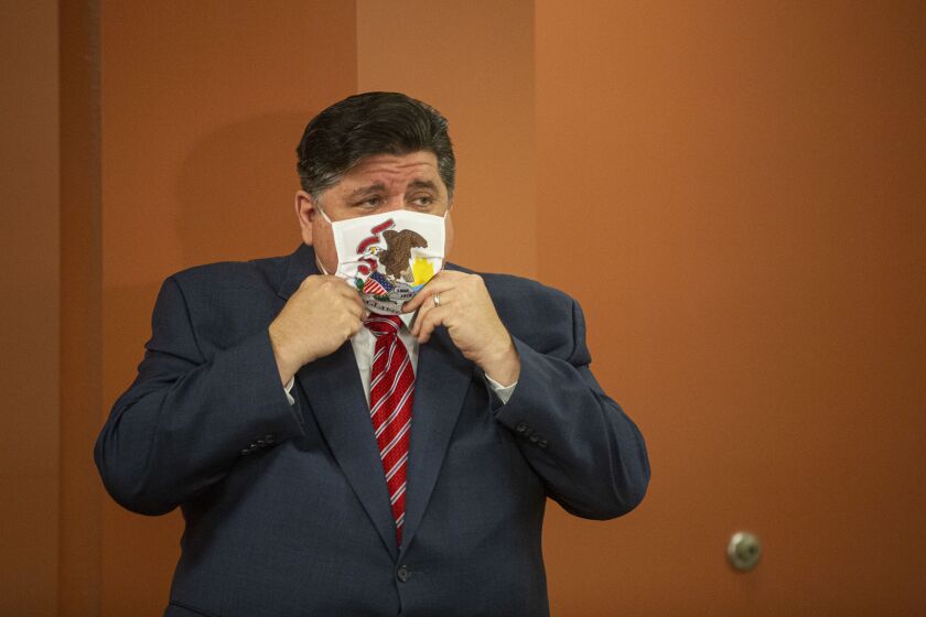 Gov. J.B. Pritzker adjusts his mask during a Chicago news conference in July.