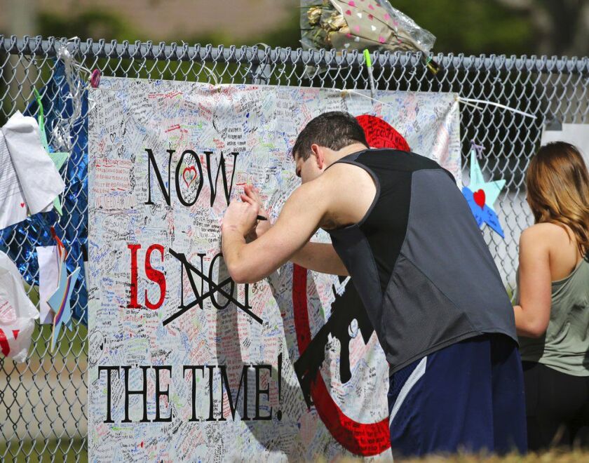 A man signs a banner as people pay tribute at a memorial for the victims of the shooting at Marjory Stoneman Douglas High School on Sunday in Parkland, Fla. Thousands of students joined their parents in walking past the three-story building at the Florida