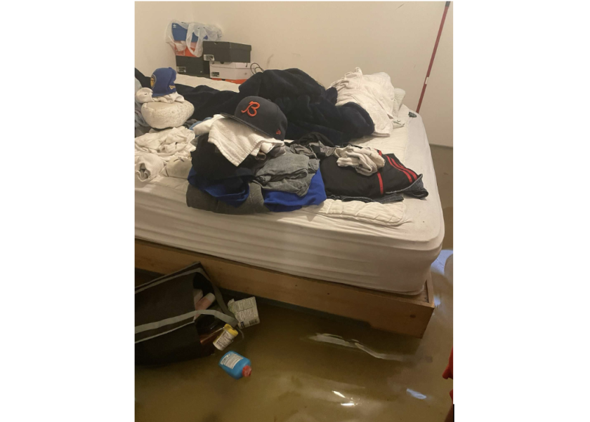 Inches of water surrounding a bed in a basement. The bed has clothes piled on it.