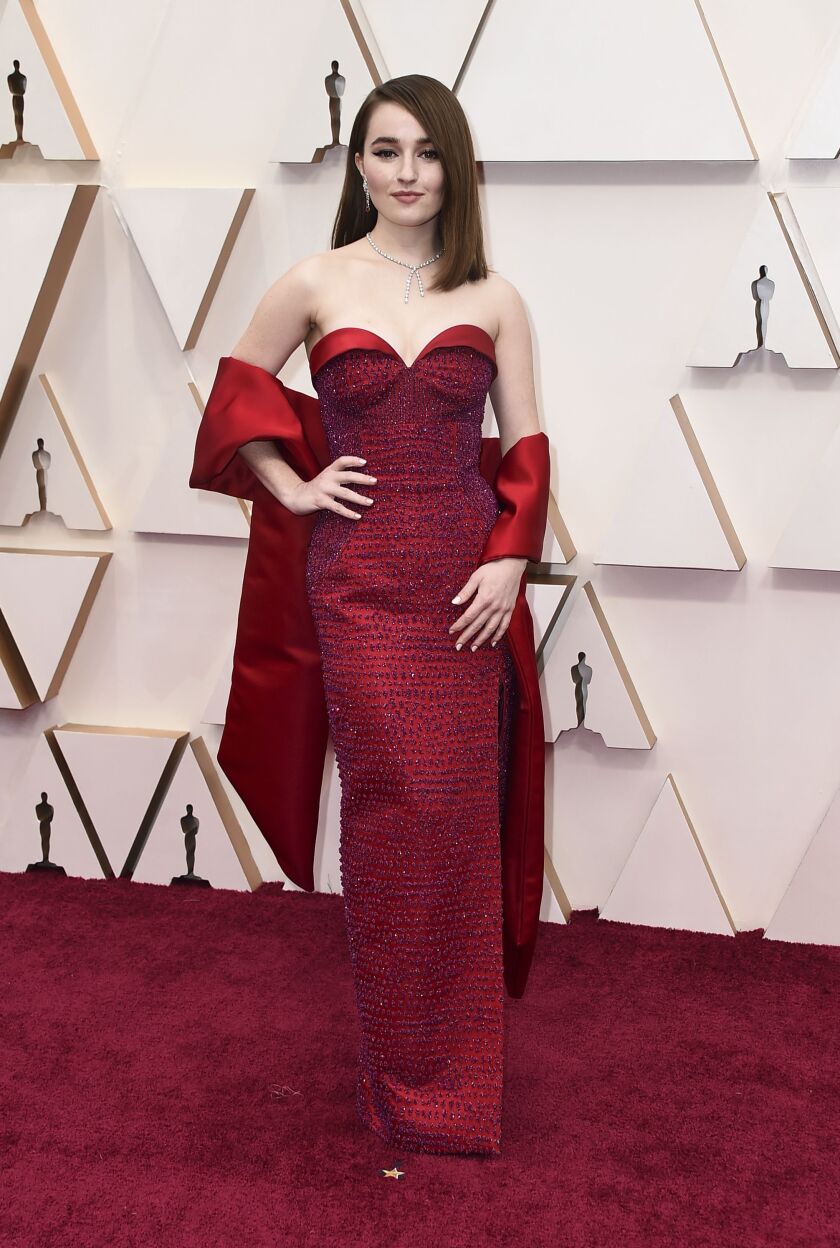 Kaitlyn Dever arrives at the Oscars wearing a scarlet Louis Vuitton couture gown designed with fuchsia glass beads and more than 14,000 Swarovski crystals.