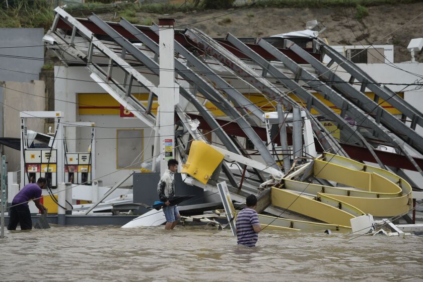 People walk next to a gas station flooded and damaged by Hurricane Maria, which hit the eastern region of the island, in Humacao, Puerto Rico, on Wednesday. The strongest hurricane to hit Puerto Rico in more than 80 years destroyed hundreds of homes, knoc