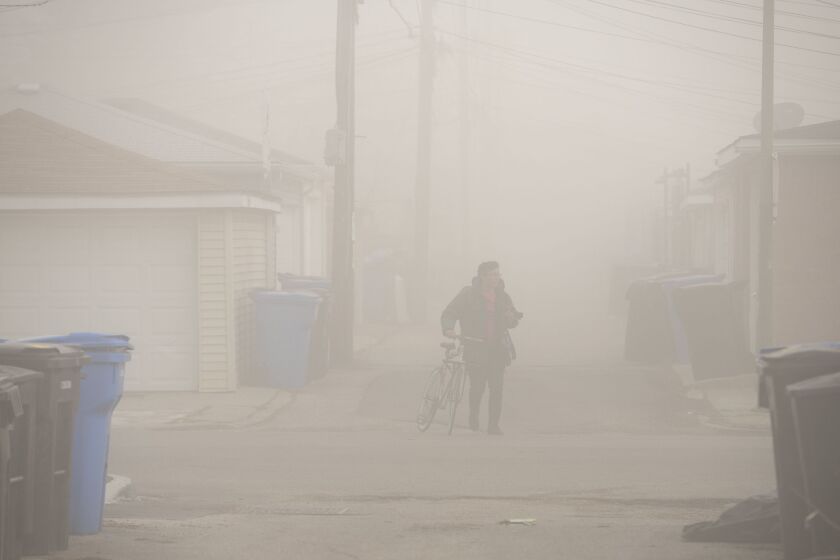 A photographer walks his bicycle though the dust cloud descending on the Little Village neighborhood after the Crawford Coal Plant smoke stack was imploded, Saturday, April 11, 2020.