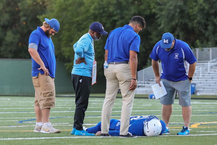 A Mather football player lays injured on the field as coaches and a referee look on during the game against Hyde Park.