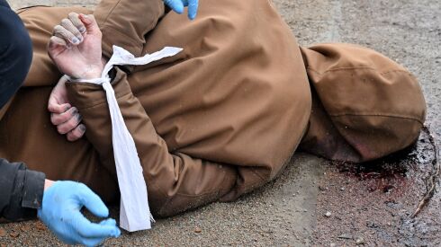 A worker releases the wrists of a dead man, his hands tied behind his back, in the town of Bucha, near the Ukrainian capital Kyiv, on April 3, 2022. Some 400 civilian bodies have been found in areas abandoned by Russian invaders.