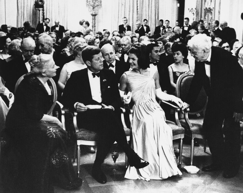 President John F. Kennedy sits with first lady Jacqueline Kennedy as poet Robert Frost, right, and Pearl Buck, left, exchange greetings in the East Room of the White House in 1962. A year earlier, Frost spoke at President Kennedy’s inaugural.