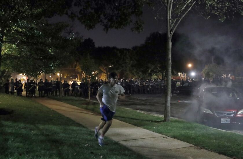 A protester runs from the police Friday in St. Louis, as protesters rally around the home of St. Louis Mayor Lyda Krewson. | Jeff Roberson/Associated Press