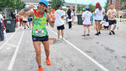 A female runner holds her medal near a race finish line.