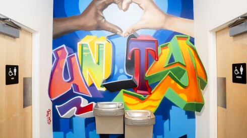 A mural showing a black hand and a white hand forming a heart above the word "Unity" over drinking fountains at the Touch Gift Foundation office.