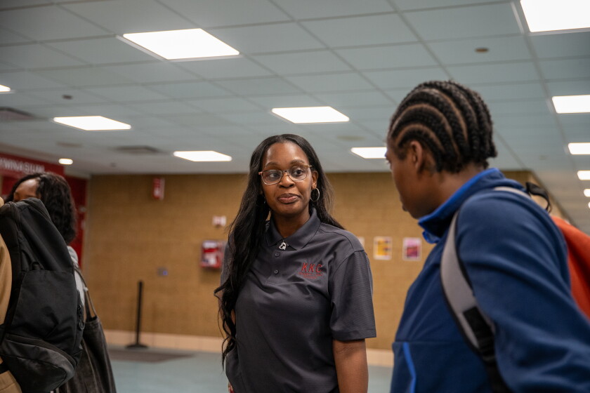 A Black woman wearing glasses speaks with a classmate at her college.