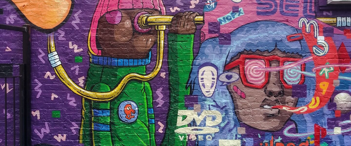 “Dumb” Donald Parker — a character from the TV show “Fat Albert and the Cosby Kids” — stands next to a floating blue-haired head. Artists JoeyD and Dredske, two of the five artists who worked on the mural at the Bridgeport restaurant Kimski, painted them. The two figures are surrounded by references to 1980s and 1990s pop culture.