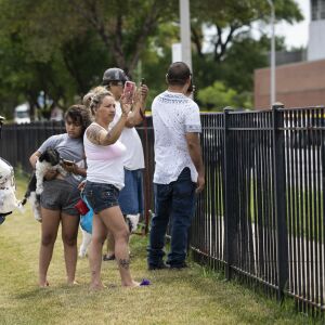 People watch from a nearby park as Chicago Police investigate at the 25th District station, 5555 W. Grand Ave., on the Northwest Side, after multiple officers were shot outside the station, Thursday morning, July 30, 2020. The suspect was also shot multiple times in the incident.