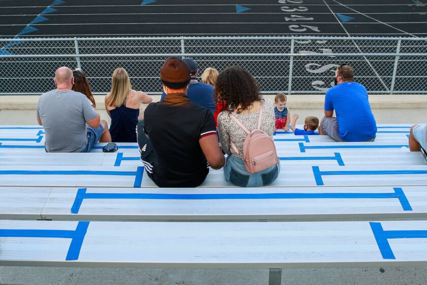 Fans sit in the stands between lines of blue tape marking 6-feet of distance during the game between Lake Central and Munster.