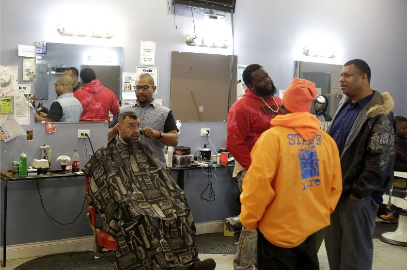 Customers at the Dana Dane Show Barber and Beauty Shop talk with CeaseFire supervisor Jowwaine Washington (orange jacket) as barber Dana Dane cuts another customer’s hair. | Joshua Lott / The Trace