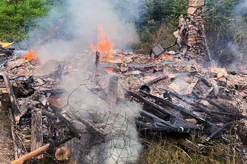 Smoke rises Aug. 4 from the burnt remains of a cabin in Canterbury, N.H., inhabited by 81-year-old David “River Dave” Lidstone, who for 27 years has lived in the woods of New Hampshire along the Merrimack River in the solar-paneled cabin.