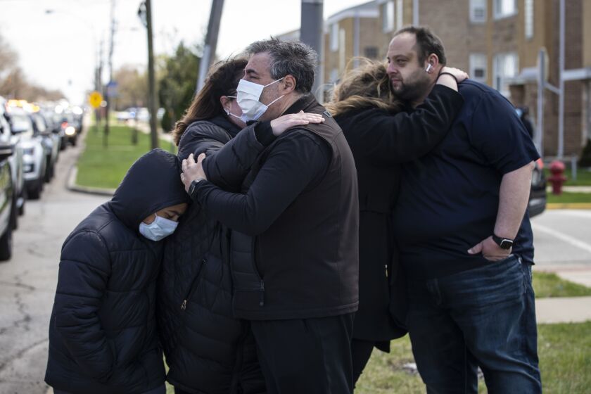 Close friends of Chicago Police Officer Marco DiFranco, who had to stand outside during the funeral amid fears of the coronavirus pandemic, hug each other as the hearse leaves Cumberland Funeral Chapels and heads toward the cemetery, Thursday, April 9, 2020.