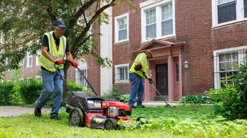 Billy "Rap" Brown mows the yard outside of a Kenwood residential building, as Malki Brown, owner of commercial landscaping firm MGE Property Solutions, trims the weeds.