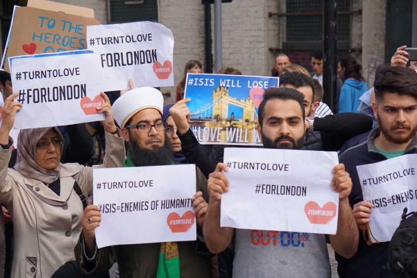 Muslims hold signs saying “ISIS WILL LOSE” and “#TURNTOLOVE” on Sunday June 4, 2017, at the police cordon surrounding the site in south London of the deadly van-and-knife attack that killed several people on Saturday night. | Raphael Satter/AP