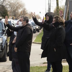 Family and friends of Chicago Police Officer Marco DiFranco, who had to stand outside during the funeral amid fears of the coronavirus pandemic, wave goodbye as the hearse leaves Cumberland Funeral Chapels and heads toward the cemetery, Thursday, April 9, 2020.