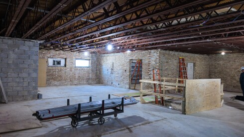 An open space under construction with exposed ceilings, ladders against the brick walls and other construction equipment.