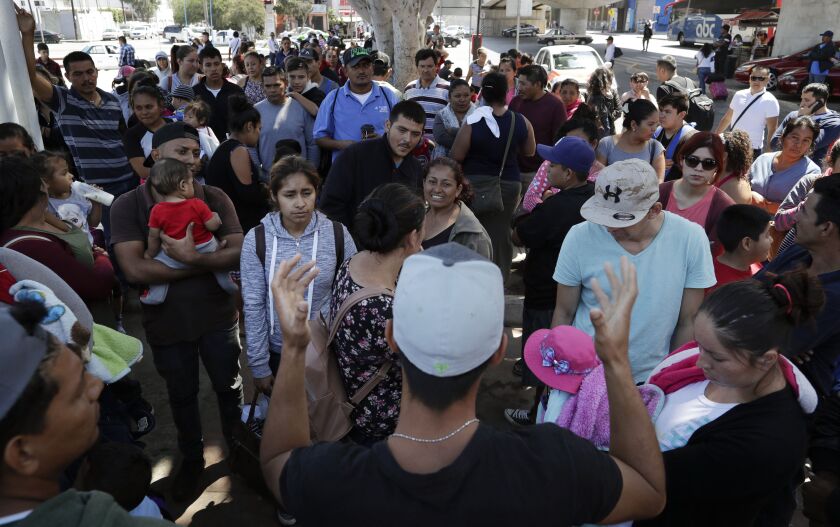 In this June 13, 2018 photo, an organizer, foreground, speaks to families as they wait to request political asylum in the United States, across the border in Tijuana, Mexico. In Tijuana, Latin Americans fleeing drug violence in their countries are camped