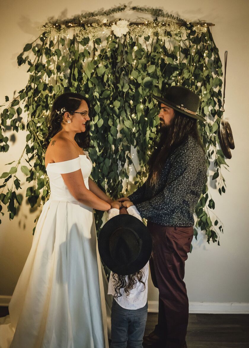 In this Dec. 2020, photo provided by Kristen Pritchard Photography, Kayleigh and Cody Cousins hold hands during their wedding ceremony, accompanied by their son, River, at home in San Diego, Calif. They initially planned an April 2020 wedding, postponed it after the pandemic took hold, rescheduled it for December, then had to shift gears again when a new lockdown was imposed. “That was devastating,” said Kayleigh. “We said, ‘Let’s just do it on Zoom.’” 