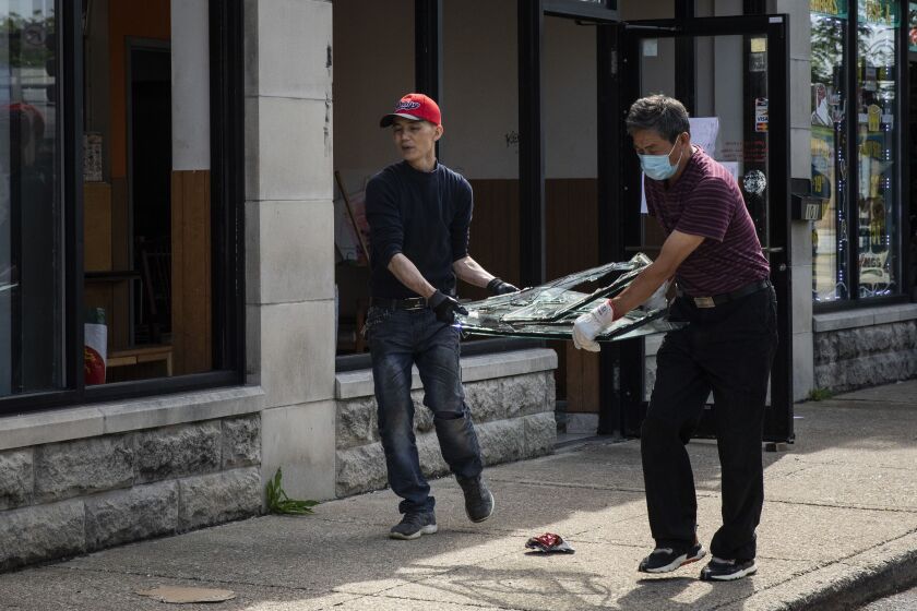 The owners of Little Wok at 103 E. 51st St. in Washington Park carry a broken window out of the restaurant Monday after it was looted over the weekend.