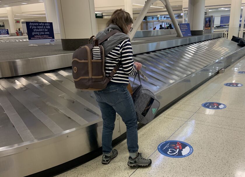 Maureen Cassidy, of Los Angeles, grabs her luggage off the baggage claim at Midway International Airport Monday, July 7, 2020. Cassidy was already planning to self-quarantine for two weeks even before Chicago issued its new travel order, which took effect Monday.