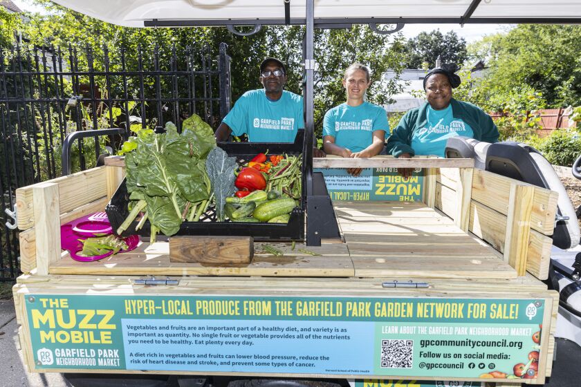 Sam Taylor, left, Nonna Ethington, and Angela Taylor, right, stand with Farmers Market on Wheels Tuesday, a golf cart dedicated to produce produce, at Fulton Street Flower and Vegetable Garden on the west side.