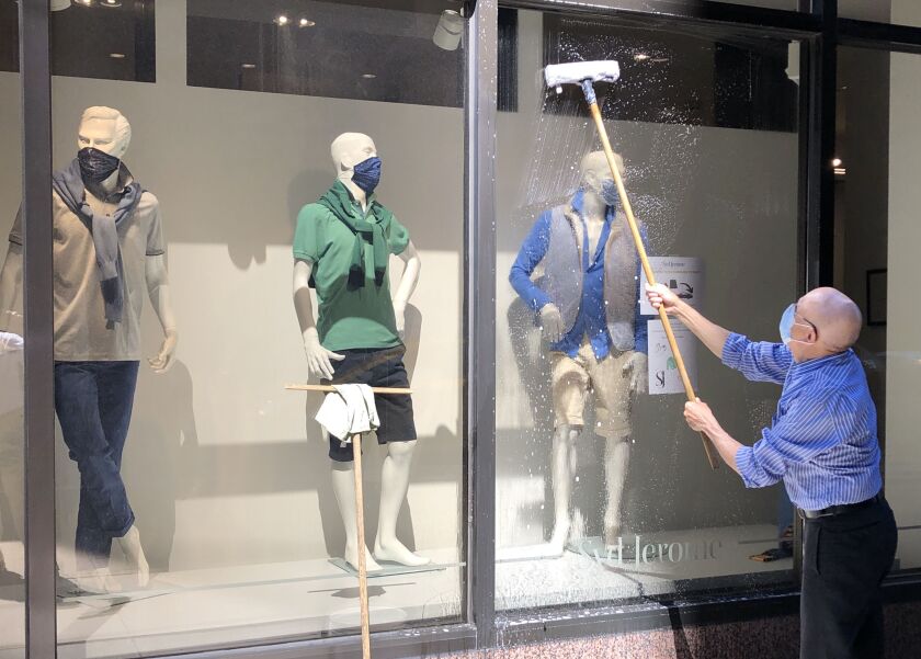 Even the mannequins wear masks at Syd Jerome, a men’s clothing store in the Loop. Employee Carlos Nava was cleaning a window Friday in preparation for re-opening. The store was damaged during weekend looting, but this window was spared.