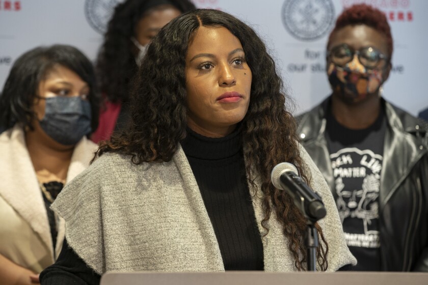 Stacy Davis Gates stands at a podium with people behind her.