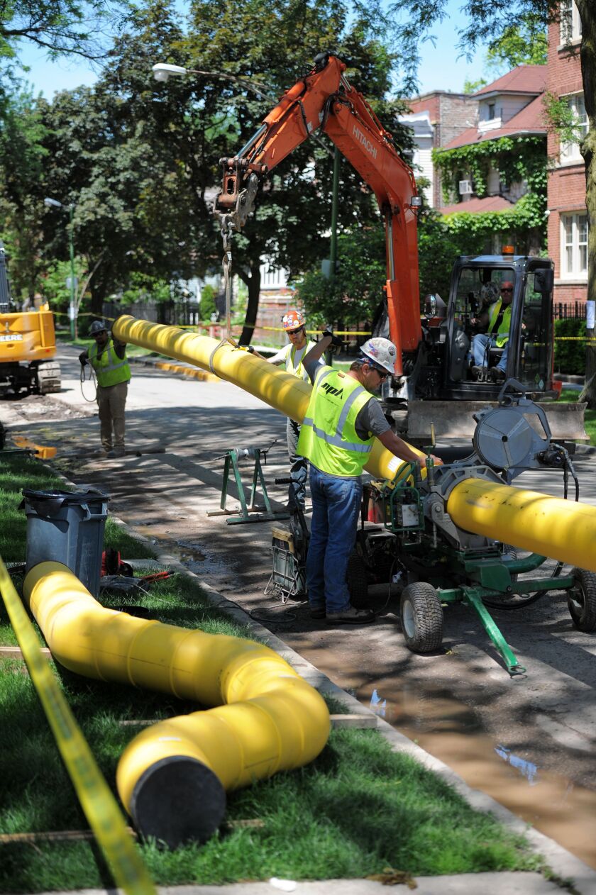 Workers stand over new gas pipelines to be installed on an Albany Park street in a photo taken last summer. Spending for the project has ballooned over the years and could ultimately cost $8 billion to $11 billion.