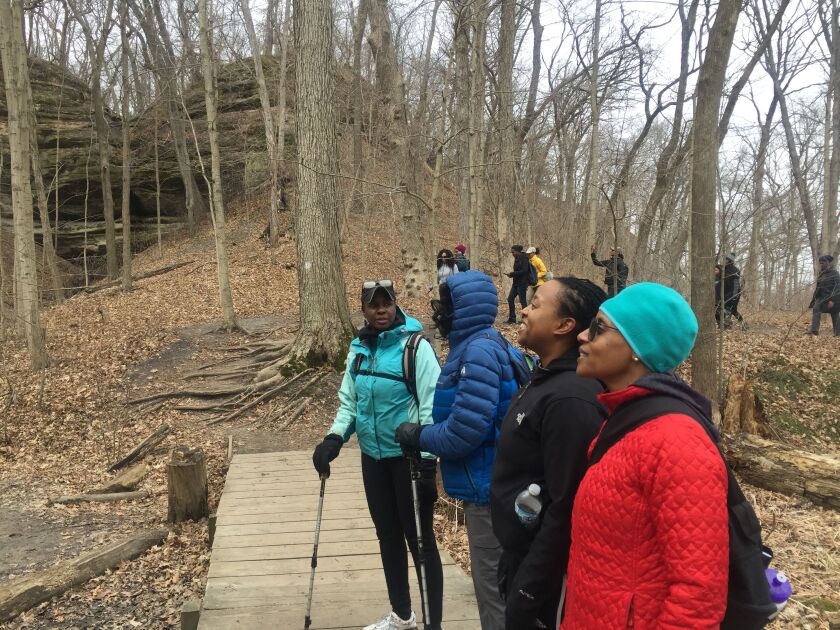 Four people in hiking gear, jackets and hats stand look out to the left and smiling- behind them are bare trees in a winter landscape.