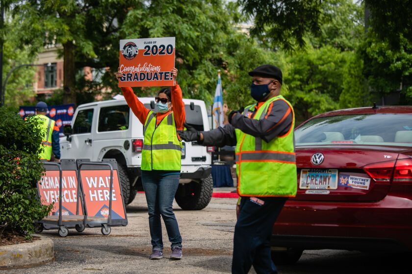 Ushers cheer and dance for graduates during a drive-thru graduation for Whitney Young Magnet High School students in June.