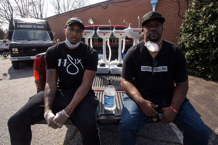 Grammy award-winning hip hop recording artist Lecrae, left, and Love Beyond Walls founder Terence Lester, right, sit on a truck bed filled with portable wash stations on Thursday, March 19, 2020 in College Park, Georgia.